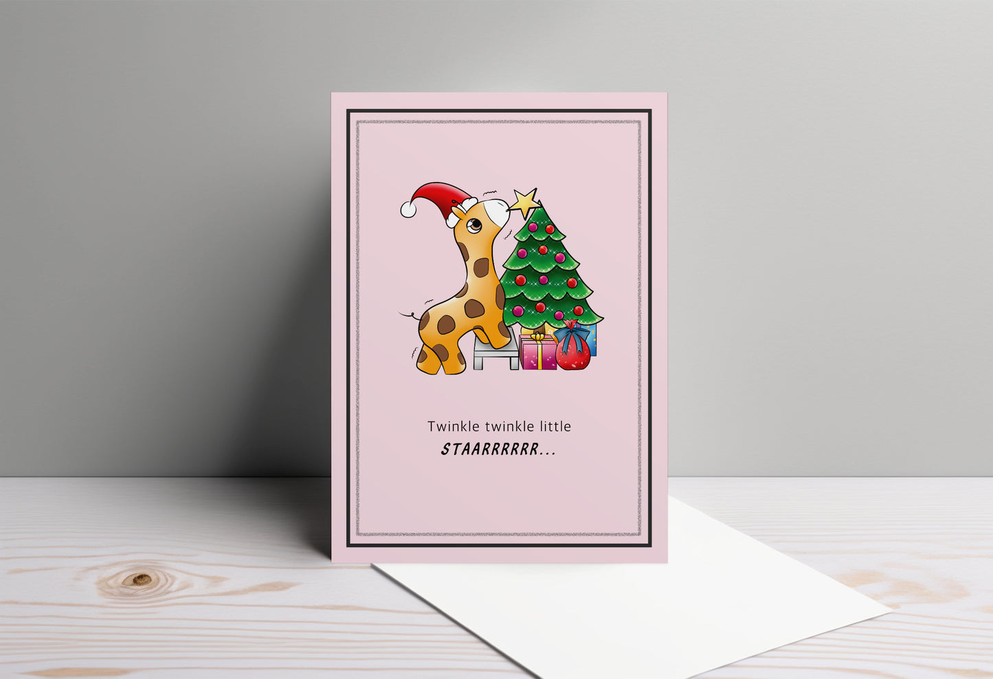 A kawaii greeting card from Rainbow & Bubbles, showing a baby giraffe with. santa hat struggling to put the star on the Christmas tree.