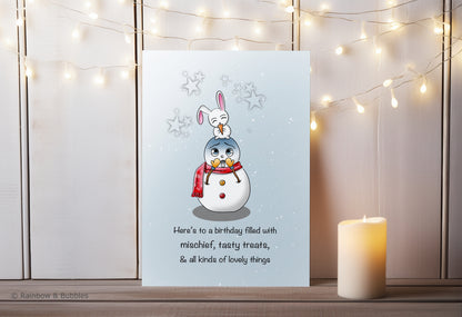 A kawaii birthday card from Rainbow & Bubbles, showing a mischievous bunny eating a tasty treat (the snowman's nose).