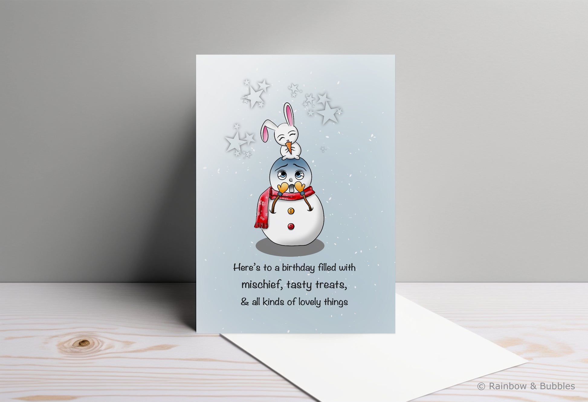 A kawaii birthday card from Rainbow & Bubbles, showing a mischievous bunny eating a tasty treat (the snowman's nose).